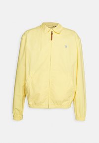 Gelbe leichte Jacke mit einem Kragen, Frontreißverschluss und elastischen Bündchen. Verfügt über Seitentaschen und ein kleines Logo auf der Brust.