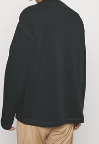 Sweatshirt gris foncé avec des manches raglan, orné de coutures contrastées et d'un col rond. Coupe ample et tissu doux et texturé.