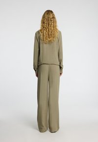 Ensemble deux pièces kaki comprenant un haut à manches longues et un pantalon large en tissu texturé. La vue de dos montre une coupe ample et un léger éclat.