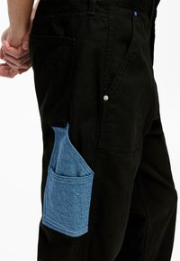 Pantaloni negri cu detalii din denim albastru la buzunar, având un material texturat, nasture tip snap și un design clasic.