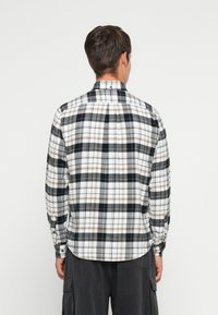 Ilgų rankovių plaid marškiniai balta, juoda ir ruda spalvomis. Yra su mygtukų apykakle, nugaros raukiniu ir reguliuojamais mygtukais ant rankovių, bei apvaliu kraštu.