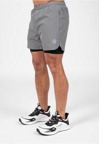 Grijze sportshorts met een elastische tailleband, zijzakken en een zwarte binnenvoering, gecombineerd met zwart-witte hardloopschoenen.