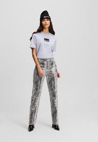 Svetlofialové tričko s okrúhlym výstrihom a čiernou nášivkou, kombinované so snake print nohavicami v odtieňoch sivej a čiernymi lesklými členkovými čižmami.