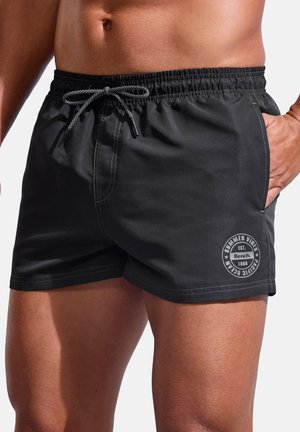 Black swim shorts made from lightweight material, featuring an elastic waistband with a drawstring and a round logo detail on the left leg.