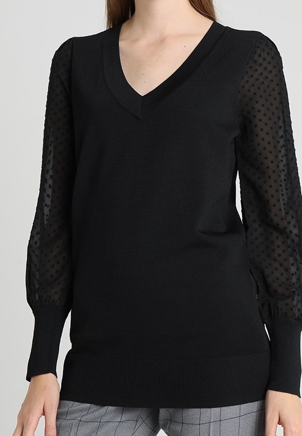 Pull-over noir à col en V, corps uni, manches bouffantes transparentes à texture ponctuée. Matière en tricot doux avec détails côtelés.