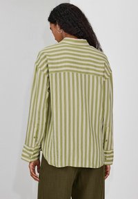 Camisa de manga larga a rayas verdes y crema, con puño abotonado y bajo ligeramente curvado, con un acabado de tela texturizada.