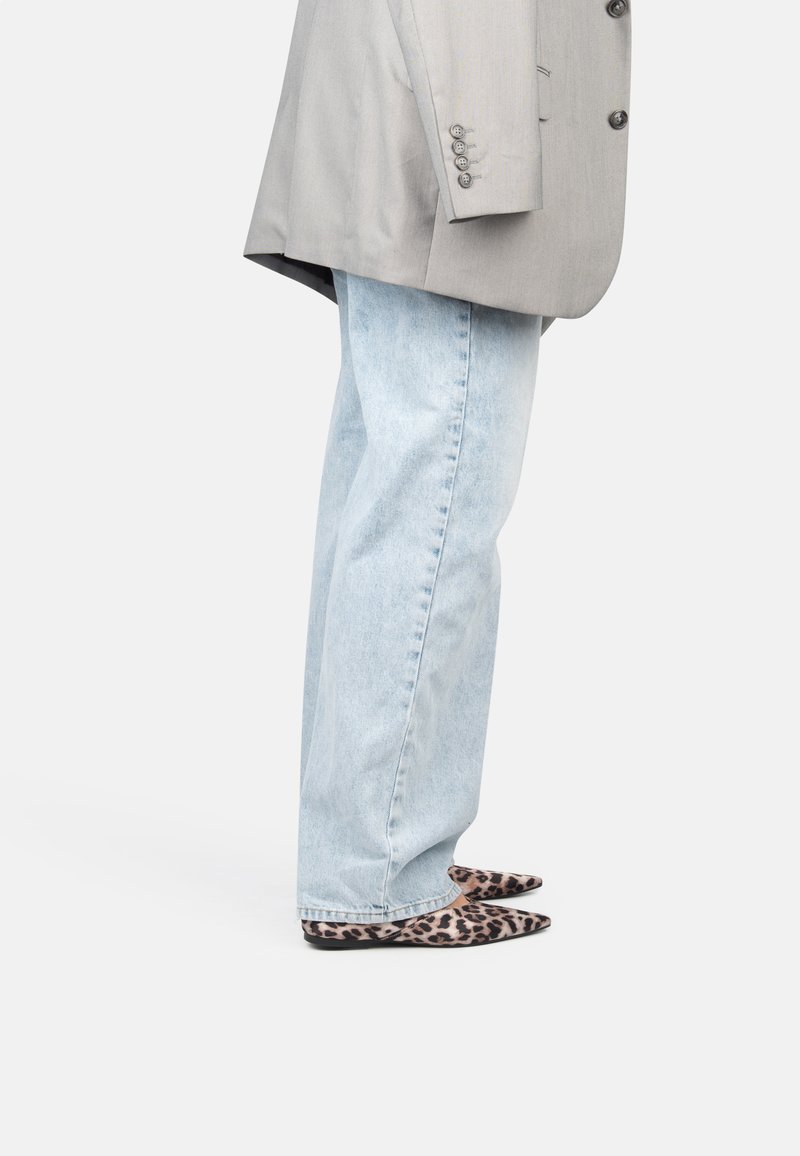 Zapatos planos de punta con estampado de leopardo, combinados con vaqueros de pierna recta en azul claro y una blazer gris claro con botones y hombros estructurados.