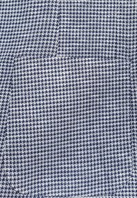 Materiał w biało-granatową kratę houndstooth o gładkiej teksturze, z małą kieszonką po lewej stronie.