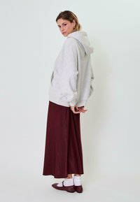 Pelēks pārāk liels kapuces džemperis, kombinēts ar garu bordo svārku un sarkanām kurpēm, akcentēts ar baltiem potīšu zeķēm. Mīksta auduma faktūras.