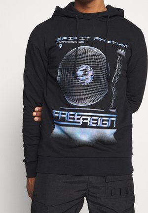 Person trägt schwarzen Kapuzenpullover mit blauem Rasterkugel-Design und den Texten "SPIRIT RHYTHM" und "FREE REIGN" auf der Vorderseite.