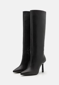 Czarne, sięgające do kolan kozaki wykonane z gładkiej skóry, z zakrzywionym noskiem i smukłym, wysokim obcasem typu szpilka. Charakteryzują się minimalistycznym designem i brakiem ozdób.