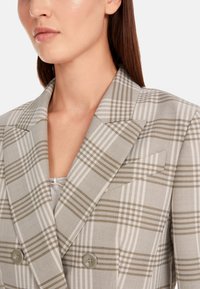 Doppelreiher-Blazer in Hellgrau mit einem Karomuster, das beige und weiße Linien umfasst. Glattes Material mit Revers und Knopfdetails.