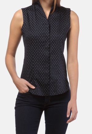 Czarna bluzka bez rękawów z małymi białymi wzorami paisley, noszona przez osobę z jedną ręką w kieszeni i w ciemnych spodniach.