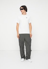 Tricou alb din bumbac cu mâneci scurte și un mic logo; pantaloni cargo gri cu multiple buzunare; adidași albi; ochelari de soare negri.