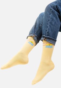Żółte skarpetki o prążkowanej fakturze zdobi wzór jasnoniebieskiej chmury oraz żółtego słońca, podkreślony pastelowymi paskami w górnej części.
