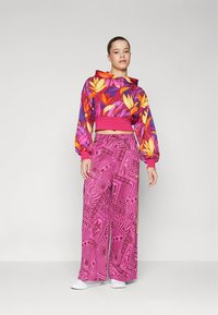 Élénk színű, virágmintás, rövidített kapucnis pulóver rózsaszín, narancssárga és sárga színekben. Laza szabású rózsaszín nadrág geometriai mintákkal és sárga kiemelésekkel.