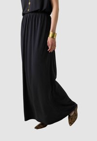 Zwarte maxi rok met een elastische tailleband, gemaakt van zachte stof. Gecombineerd met puntige schoenen met een slangenhuidpatroon. Gouden manchette armband.