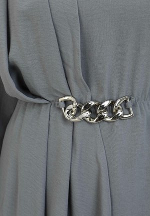 Gray fabric drapes with a loose fit. A metallic silver chain belt cinches at the waist, adding contrast with a smooth texture.