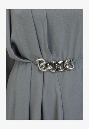 Grauer Stoff mit lockerer Passform. Ein metallic-silberner Kettengürtel betont die Taille und setzt einen Kontrast mit seiner glatten Textur.