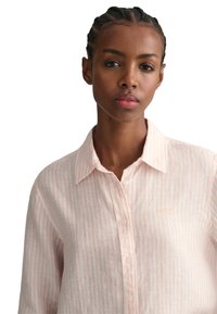 Hellrosa, gestreiftes Button-Down-Hemd aus leichtem Stoff; mit Kragen, weißen Knöpfen und einem kleinen Logo auf der Brust.