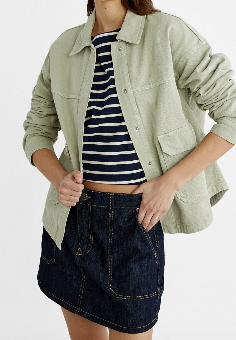 Lys grøn, knap-op jakke med en blød tekstur, parret med en marineblå og hvidstribet crop top og en mørk denim mini skirt.