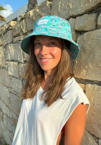 A turquoise bucket hat with a flamingo pattern, featuring a wide brim and a logo patch. The texture is smooth, suitable for sun protection.