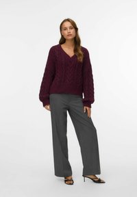 Pull en maille torsadée bordeaux avec un col en V, associé à un pantalon large gris clair et des sandales noires à talons. Texture lisse, coupe décontractée.