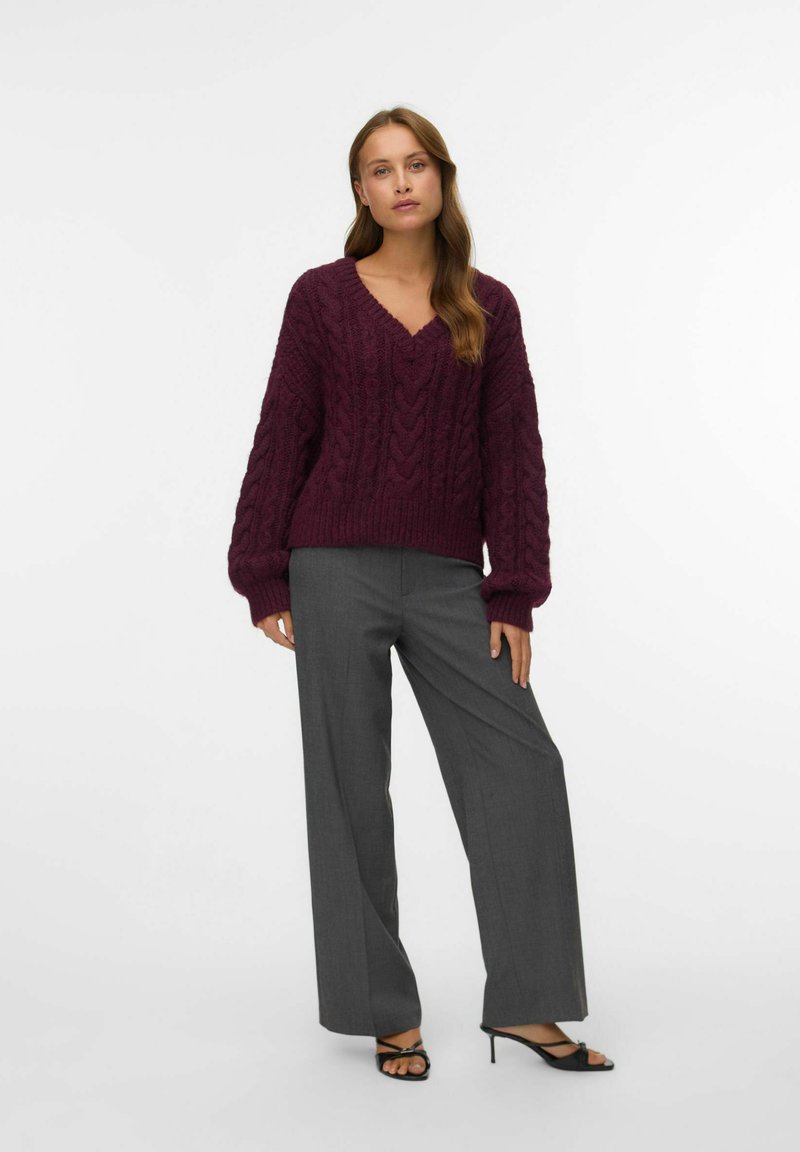 Pull en maille torsadée bordeaux avec un col en V, associé à un pantalon large gris clair et des sandales noires à talons. Texture lisse, coupe décontractée.