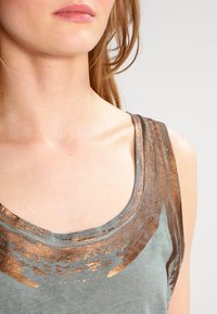 Sleeveless top in muted green fabric featuring a metallic bronze pattern along the neckline. Soft texture with a relaxed fit design.