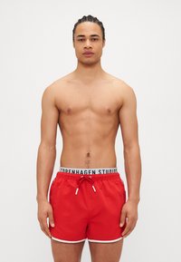 Red swim shorts with a white trim and adjustable drawstring. The waistband features a logoed elastic band. Material appears lightweight and smooth.