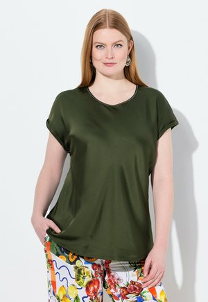 Blusa verde oliva de manga corta con cuello redondo y textura suave; combinada con pantalones coloridos y estampados que presentan motivos de frutas.