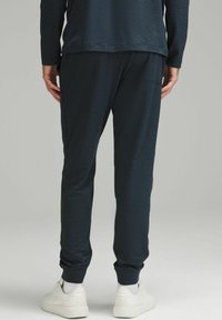 Tmavomodré tepláky vyrobené z mäkkej látky, s elastickými manžetami, bočnými vreckami a v kombinácii s bielymi teniskami pre kontrast.