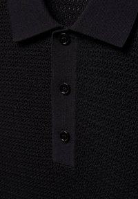 Polo en maille noire texturée avec un col côtelé et une patte de boutonnage avec trois boutons noirs.