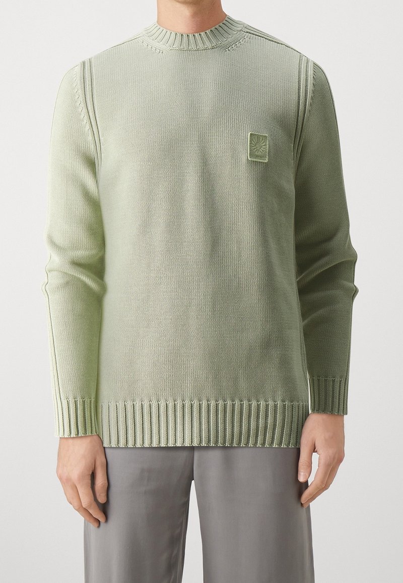 Ljusgrön stickad tröja med ribbat nederkant och ärmslut, som har ett strukturerat mönster och en liten fyrkantig logotyp på bröstet.
