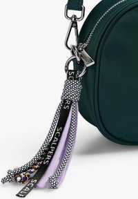 Bolso de tela verde con un clip plateado, adornado con borlas en púrpura, negro y hilos multicolores, presentando patrones tejidos.