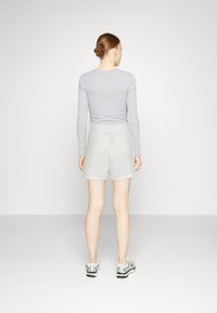 Maglietta a maniche lunghe grigia chiara abbinata a pantaloni corti di colore chiaro. L'outfit presenta una vestibilità comoda e un tessuto morbido, mettendo in mostra un design minimalista.