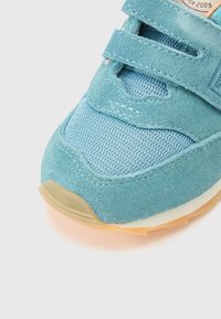 Μπλε παπούτσι από σουέτ με επενδύσεις από δίχτυ, λουριά με βέλκρο, στρογγυλεμένη καουτσούκ σόλα και διακριτικές λεπτομέρειες ραφών. Ο σχεδιασμός είναι αθλητικός και πρακτικός.