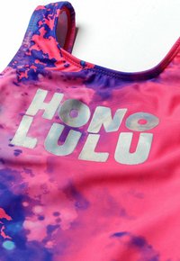 Maillot de bain tie-dye rose vif et violet avec des lettres argentées écrivant "HONOLULU." Tissu lisse et extensible avec un design classique de débardeur.