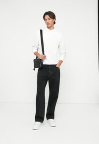 Hvit genser, svarte vide jeans og hvite sneakers. Liten svart crossover-veske med stropp. Enkelt, moderne design.