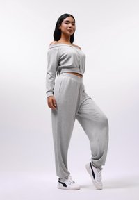 Jasnoszara, żebrowana kompletny zestaw crop topu i joggerów, z off-shoulder designem, elastycznym pasem i kieszeniami bocznymi, noszony z białymi sneakersami.