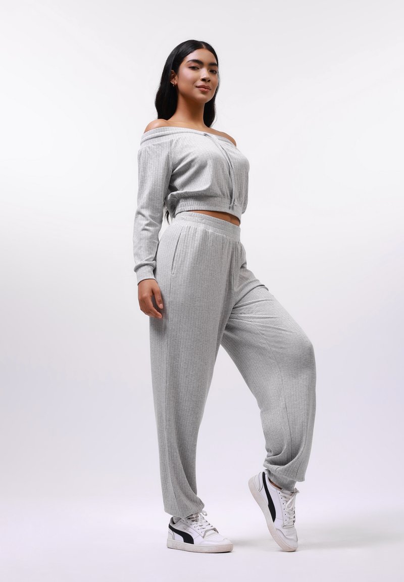 Jasnoszara, żebrowana kompletny zestaw crop topu i joggerów, z off-shoulder designem, elastycznym pasem i kieszeniami bocznymi, noszony z białymi sneakersami.