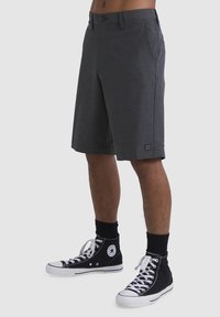Pantalones cortos informales en gris oscuro, fabricados en tejido ligero, con un diseño de frente plano, bolsillos laterales y un pequeño parche con el logo cerca del dobladillo.