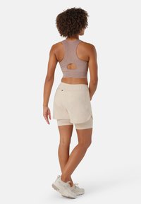 Pantalones cortos deportivos de color beige claro con un ajuste holgado, combinados con un top corto de color marrón con textura y un corte circular en la parte posterior.