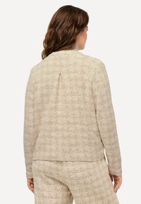 Beige jas met een gestructureerde weving met een subtiel geometrisch patroon, lange mouwen en een achterventilatie detail voor gemakkelijke beweging.