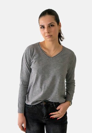 Pull en V gris en tricot doux, associé à un jean noir. Le pull a des manches longues et des accents côtelés discrets au niveau des poignets.
