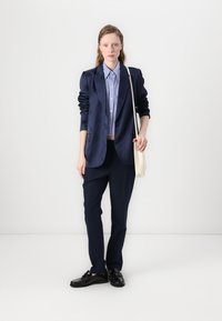 Tumesinise blazer, millel on tekstuurne kangas, koos helesinise triibulise särgi, tumedate pükste ja mustade kingadega. Ligipääsetav beež kott.