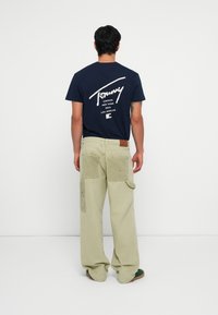 T-shirt en coton bleu marine avec un texte graphique blanc au dos, associé à un pantalon cargo beige clair avec de grandes poches.