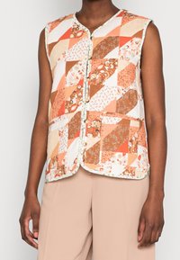 Chaleco acolchado en tonos naranjas y marrones con diseño de patchwork. Presenta un cuello redondo, botones en la parte delantera y acentos florales en los bordes.