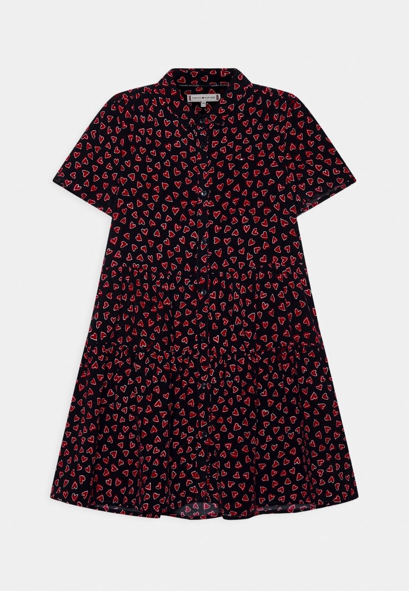 Robe noire à manches courtes avec boutons, motif de cœurs rouges, col et jupe à volants, étalée à plat sur un fond blanc.