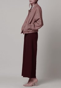 Chaqueta bomber rosa con estampado pata de gallo y puños elásticos, combinada con pantalones anchos oscuros y zapatos de tacón alto brillantes en rosa claro.